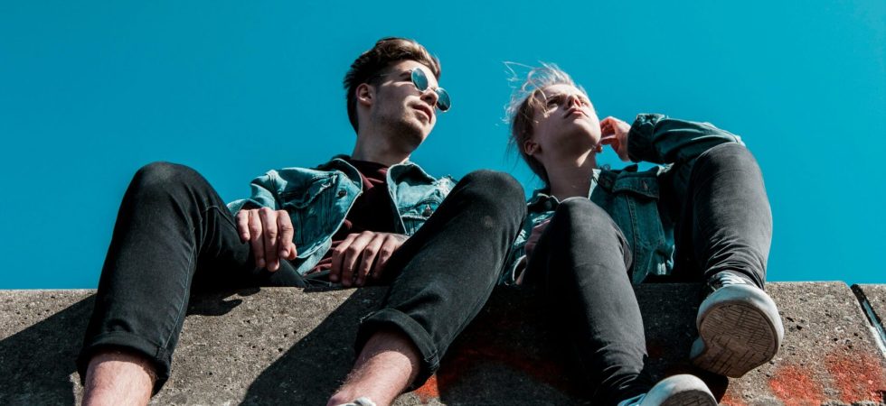 Two young people sitting on a stone wall under a vibrant blue sky, enjoying a sunny day together.